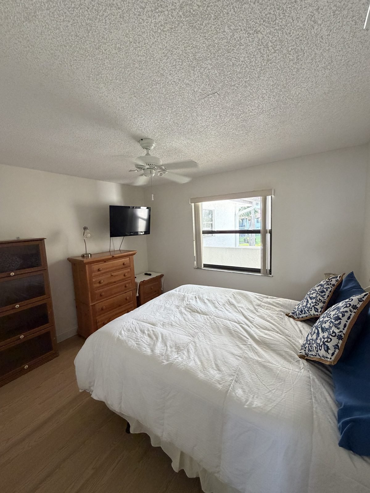 Second bedroom with a made bed, dresser, wall-mounted TV, and window